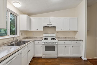 Kitchen with white appliances, white cabinetry, wood tiled floors, lofted ceiling, and a textured ceiling