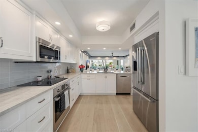 Kitchen with appliances with stainless steel finishes, light wood finished floors, a tray ceiling, white cabinetry, and backsplash