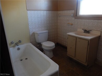 Bathroom with vanity, toilet, tile walls, tile flooring, and a bath to relax in