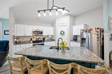 Kitchen with white cabinetry, stainless steel appliances, backsplash, light stone counters, and lofted ceiling