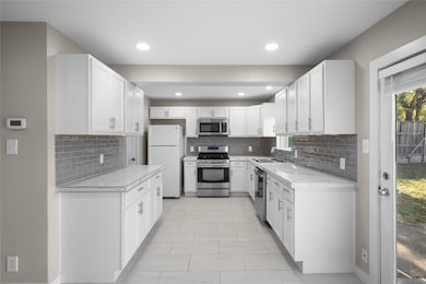 Kitchen with appliances with stainless steel finishes, white cabinets, tasteful backsplash, recessed lighting, and light tile patterned flooring