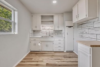 Kitchen with decorative backsplash, light wood-type flooring, white cabinets, and light countertops