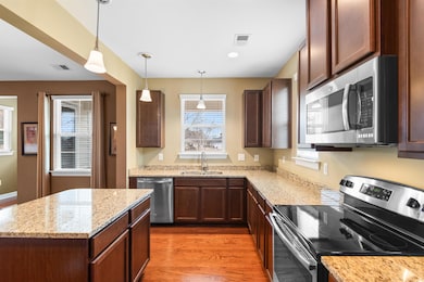 Kitchen featuring decorative light fixtures, sink, dark hardwood / wood-style flooring, light stone counters, and stainless steel appliances