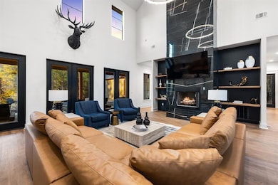 Living room with a towering ceiling, healthy amount of natural light, wood finished floors, built in shelves, and a high end fireplace