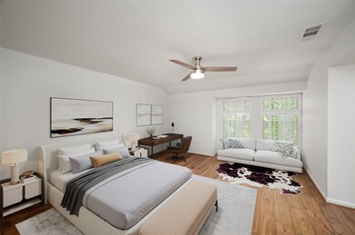 This picture was virtually staged. This spacious primary bedroom features hardwood floors, room for a king sized bed and a cozy sitting area by a window with plantation shutters. The room includes a ceiling fan and a desk area, providing a comfortable and stylish living space.