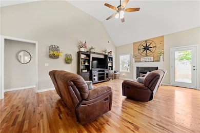 Living area with high vaulted ceiling, light wood-type flooring, ceiling fan, a fireplace, and baseboards
