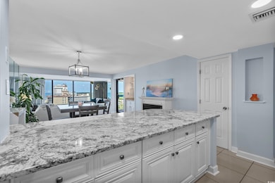 Kitchen with white cabinets, light stone countertops, light tile patterned flooring, hanging light fixtures, and a chandelier