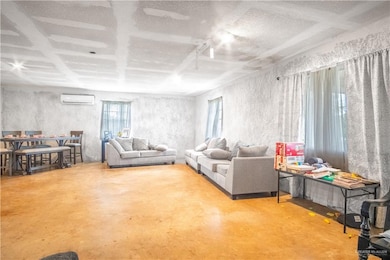 Living room featuring finished concrete floors, a wall mounted air conditioner, and a textured ceiling