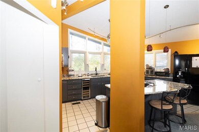 Bar area with black refrigerator with ice dispenser, light tile patterned flooring, light stone counters, beverage cooler, and pendant lighting