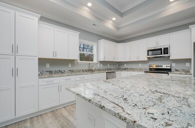 Kitchen with white cabinets, stainless steel appliances, light stone countertops, and crown molding