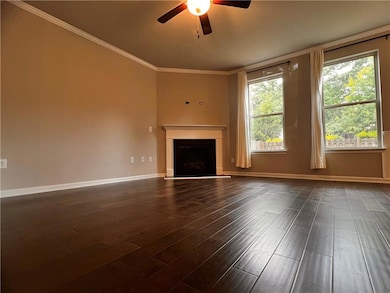 Unfurnished living room featuring ceiling fan, a fireplace, dark wood-style floors, crown molding, and baseboards