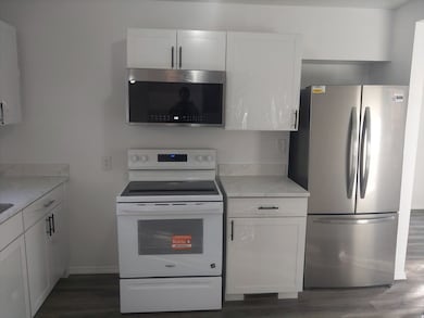 Kitchen featuring stainless steel appliances, white cabinetry, dark wood-type flooring, and light stone counters