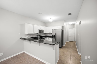 Kitchen featuring a kitchen bar, appliances with stainless steel finishes, a peninsula, white cabinets, and light tile patterned flooring