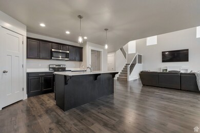 Kitchen featuring dark wood-type flooring, a breakfast bar, open floor plan, appliances with stainless steel finishes, and light countertops