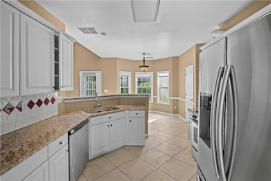 Kitchen with appliances with stainless steel finishes, a peninsula, backsplash, light tile patterned floors, and white cabinets