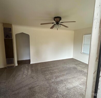 Unfurnished room featuring arched walkways, a heating unit, dark colored carpet, and ceiling fan