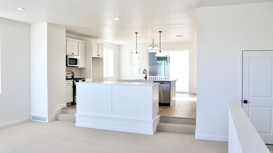 Kitchen with a center island with sink, pendant lighting, stainless steel appliances, light colored carpet, and white cabinets