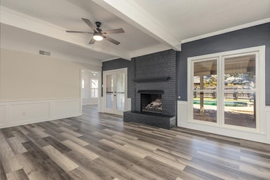 Unfurnished living room featuring a textured ceiling, a fireplace, a decorative wall, beamed ceiling, and a wainscoted wall