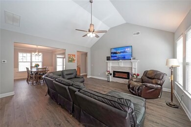 Living area with lofted ceiling, wood finished floors, a glass covered fireplace, a ceiling fan, and a chandelier