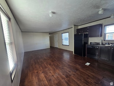 Kitchen with open floor plan, black appliances, dark wood-type flooring, a textured ceiling, and dark countertops