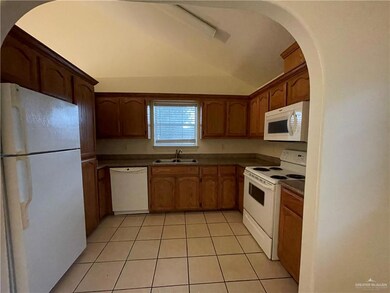 Kitchen with white appliances, light tile patterned flooring, dark countertops, lofted ceiling, and arched walkways