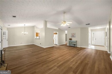 Unfurnished living room with ceiling fan, a chandelier, a textured ceiling, wood finished floors, and vaulted ceiling