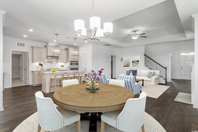 Dining space with dark wood-type flooring, a raised ceiling, and ceiling fan with notable chandelier