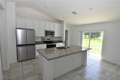 Kitchen featuring appliances with stainless steel finishes, dark stone counters, white cabinetry, backsplash, and lofted ceiling