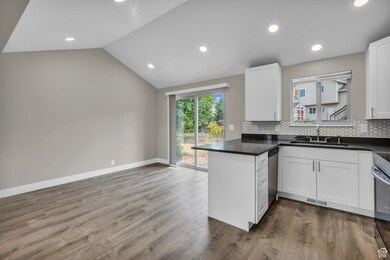 Kitchen featuring a peninsula, lofted ceiling, backsplash, white cabinetry, and recessed lighting
