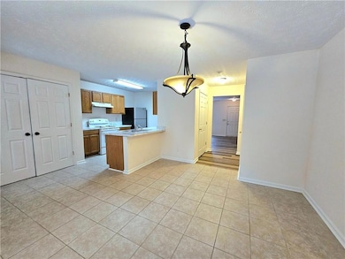 Kitchen featuring electric stove, under cabinet range hood, freestanding refrigerator, brown cabinets, and light tile patterned flooring