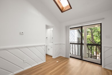 Empty room with wainscoting, healthy amount of natural light, a skylight, a decorative wall, and light wood-style flooring