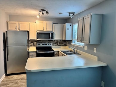 Kitchen with stainless steel appliances, a peninsula, light wood finished floors, tasteful backsplash, and light countertops