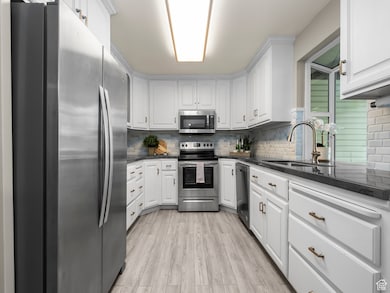 Kitchen with appliances with stainless steel finishes, dark stone counters, backsplash, and white cabinetry