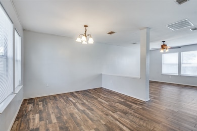 Empty room with a ceiling fan, dark wood-style flooring, and a chandelier