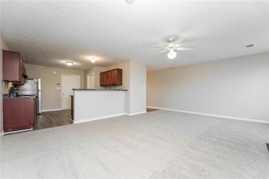 Unfurnished living room featuring dark colored carpet, a ceiling fan, and a textured ceiling