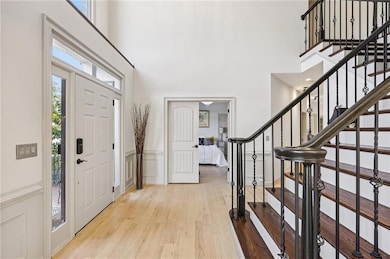 Entryway featuring healthy amount of natural light, a decorative wall, light wood finished floors, stairway, and a towering ceiling