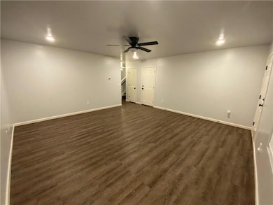 Empty room featuring dark wood-style flooring, ceiling fan, and stairway