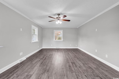 Unfurnished room with ceiling fan, healthy amount of natural light, dark wood-style floors, crown molding, and a textured ceiling