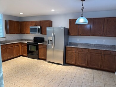 Kitchen featuring appliances with stainless steel finishes, dark stone counters, light tile patterned floors, hanging light fixtures, and recessed lighting