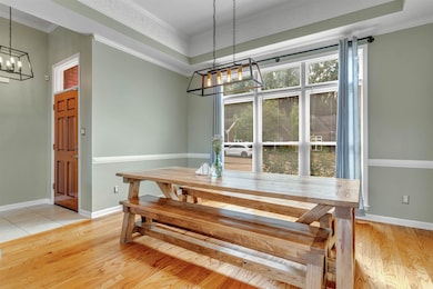 Dining area with crown molding, a chandelier, light wood-style floors, and a tray ceiling