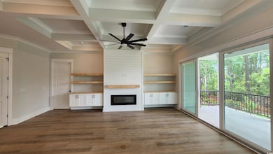 Unfurnished living room featuring ceiling fan, a large fireplace, coffered ceiling, dark wood-type flooring, and beamed ceiling