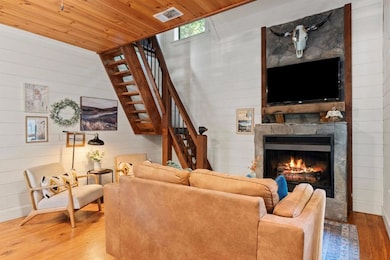 Living area with stairway, wood finished floors, wood walls, wood ceiling, and a stone fireplace