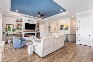 Living room with a raised ceiling, ceiling fan, light wood finished floors, a glass covered fireplace, and recessed lighting