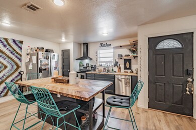 Kitchen with butcher block countertops, a textured ceiling, appliances with stainless steel finishes, a kitchen bar, and wall chimney exhaust hood