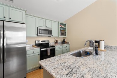 Kitchen featuring appliances with stainless steel finishes, a sink, vaulted ceiling, light stone countertops, and a peninsula