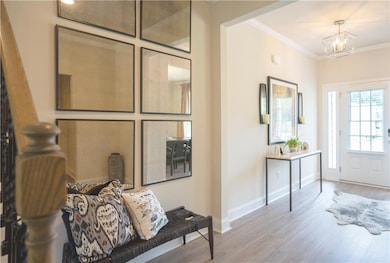 Entrance foyer with wood finished floors, crown molding, and a chandelier