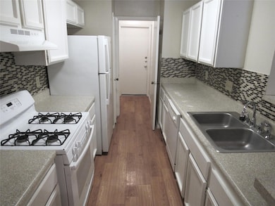Kitchen with white appliances, dark wood-type flooring, white cabinetry, decorative backsplash, and under cabinet range hood