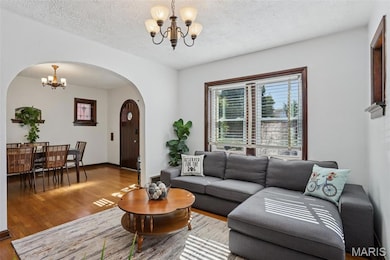 Living area with a chandelier, wood finished floors, arched walkways, and a textured ceiling