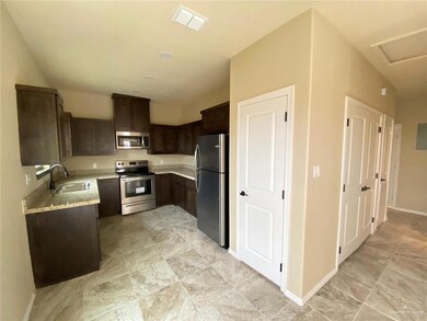 Kitchen featuring appliances with stainless steel finishes, dark brown cabinetry, light stone counters, and light stone finish floors