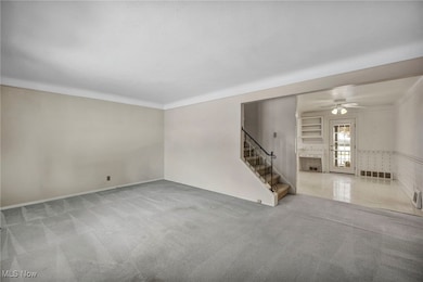 Unfurnished living room featuring carpet, stairs, a ceiling fan, and ornamental molding